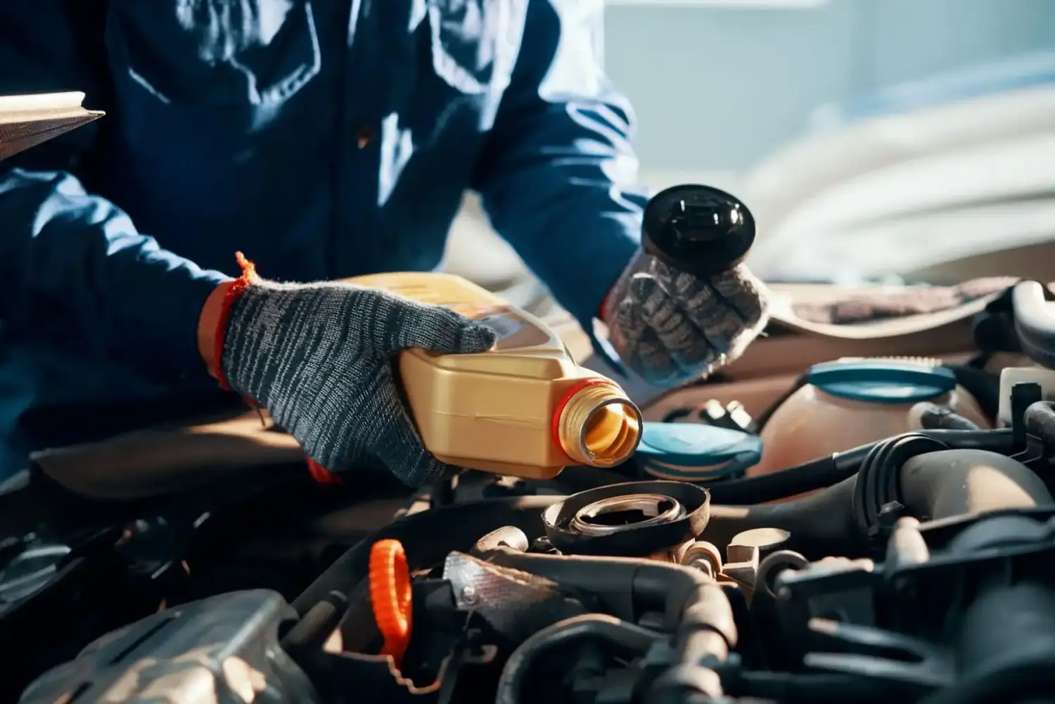 Hände eines Mechanikers gießen eine Flasche Öl in den Automotor.