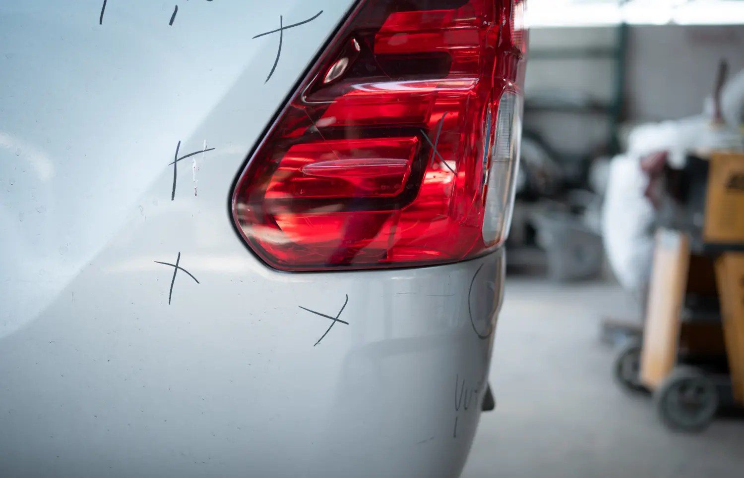 Ein Automechaniker prüft den Zustand einer Karosserie nach einem Unfall. Er markiert die zu reparierenden Stellen mit einem X.